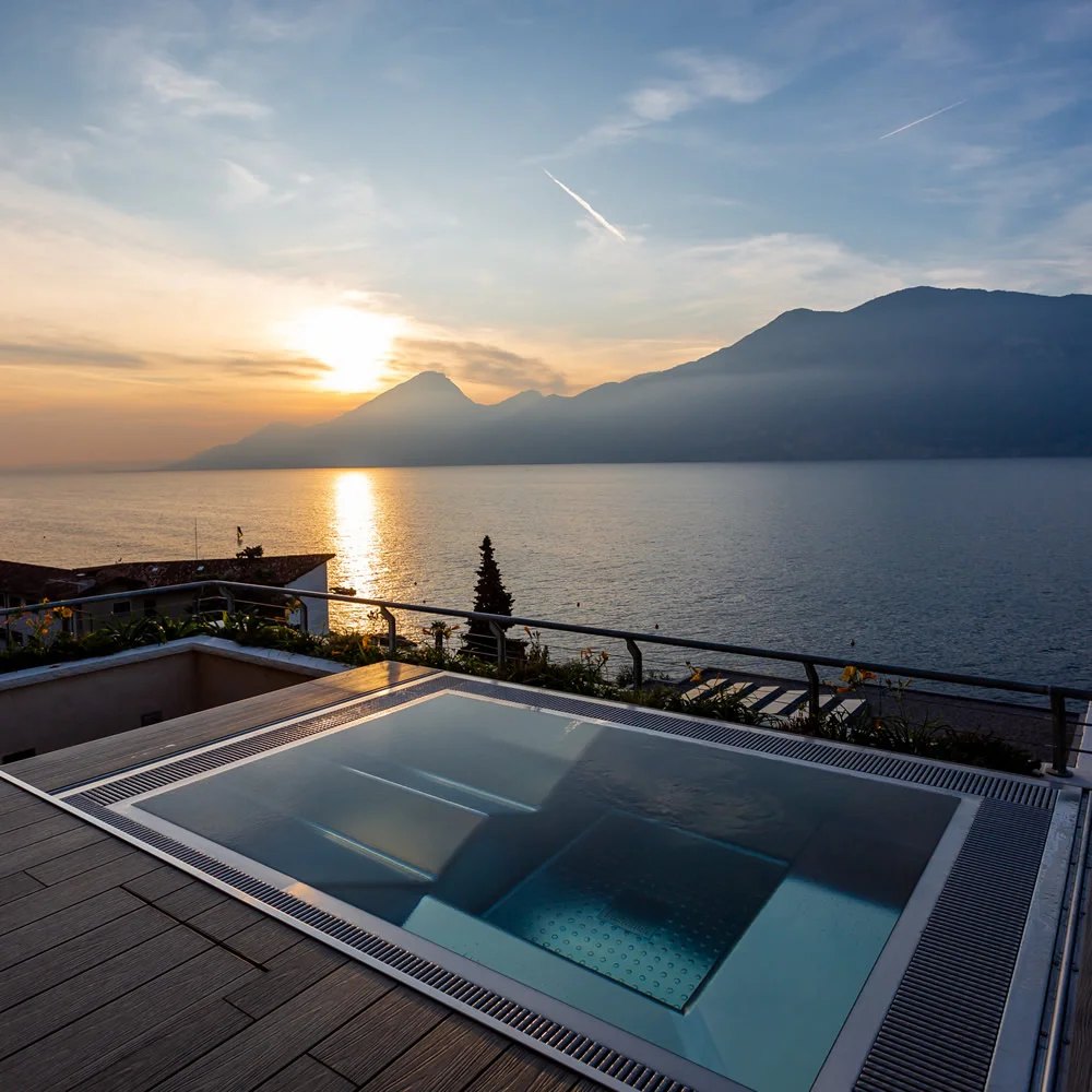 Spa H2O Style en acier inox posé hors sol sur une terrasse au bord du lac, au coucher du soleil
