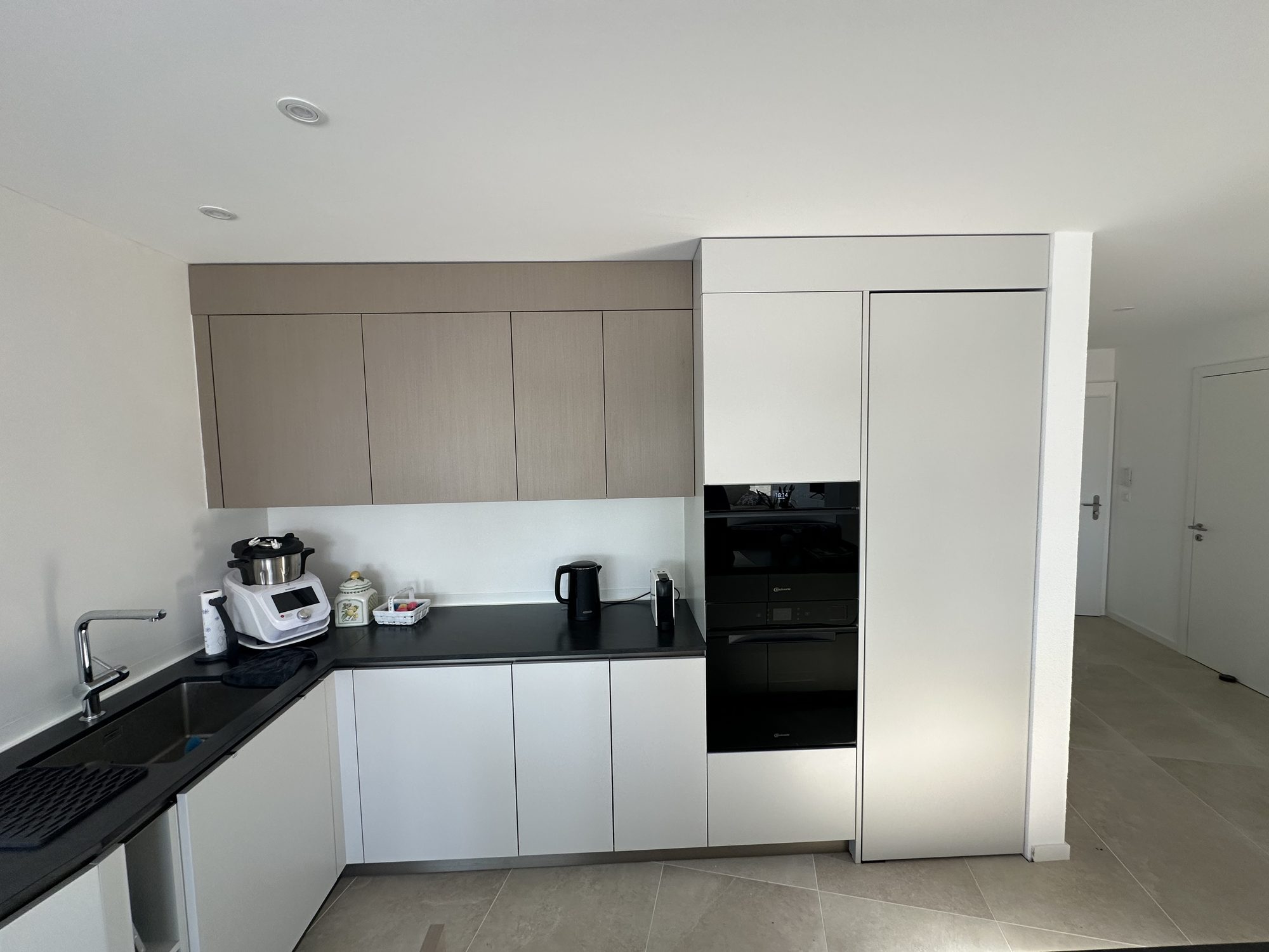 White and taupe L-shaped kitchen, black worktop