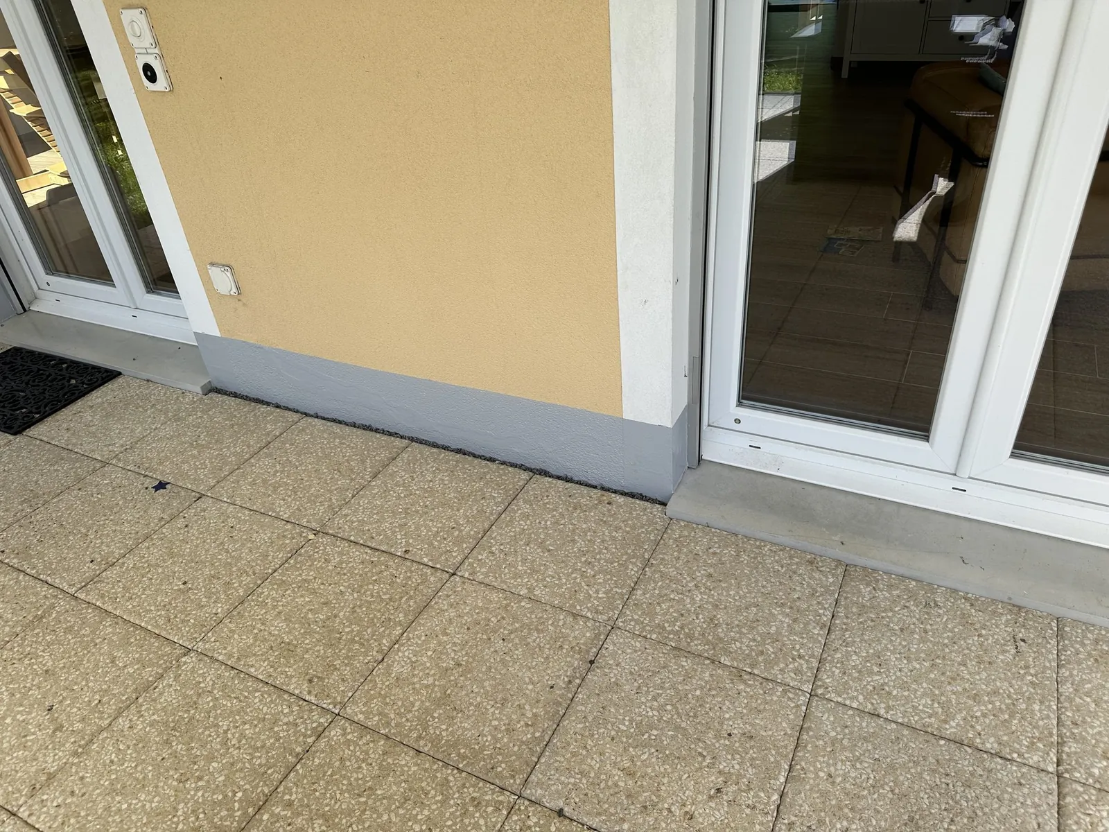 Grauer Belag am Fassadensockel entlang des Plattenbelags